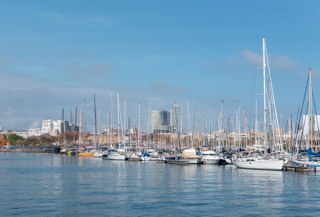 Sailboats and yachts moored in Barcelona's harbor under a blue sky