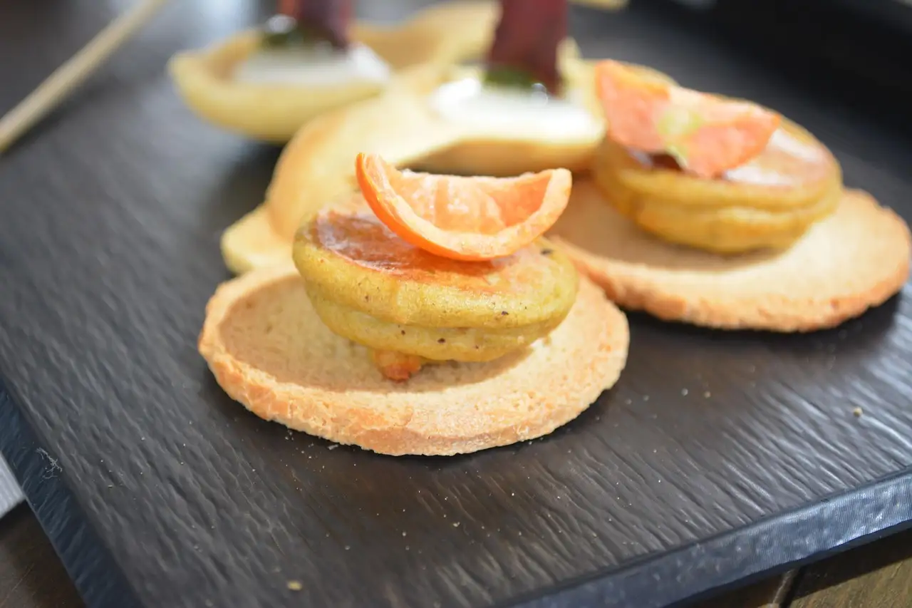 Small tapas topped with orange slices on a dark slate board