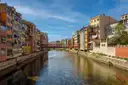 Colorful houses along the Onyar river in Girona, with a red iron footbridge