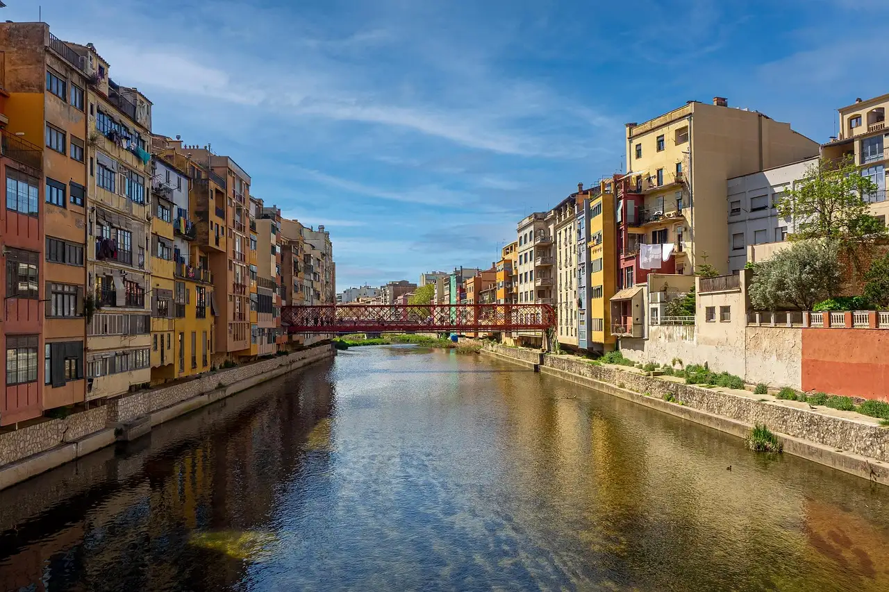Colorful houses along the Onyar river in Girona, with a red iron footbridge