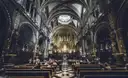 The arched, gilded nave of the Montserrat basilica, with rows of wooden pews and a few visitors