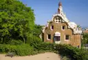 A Gaudí gatehouse at Park Güell with a wavy tiled roof and a tower, among green trees