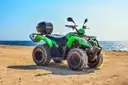 A green quad bike parked on a sandy track by the sea
