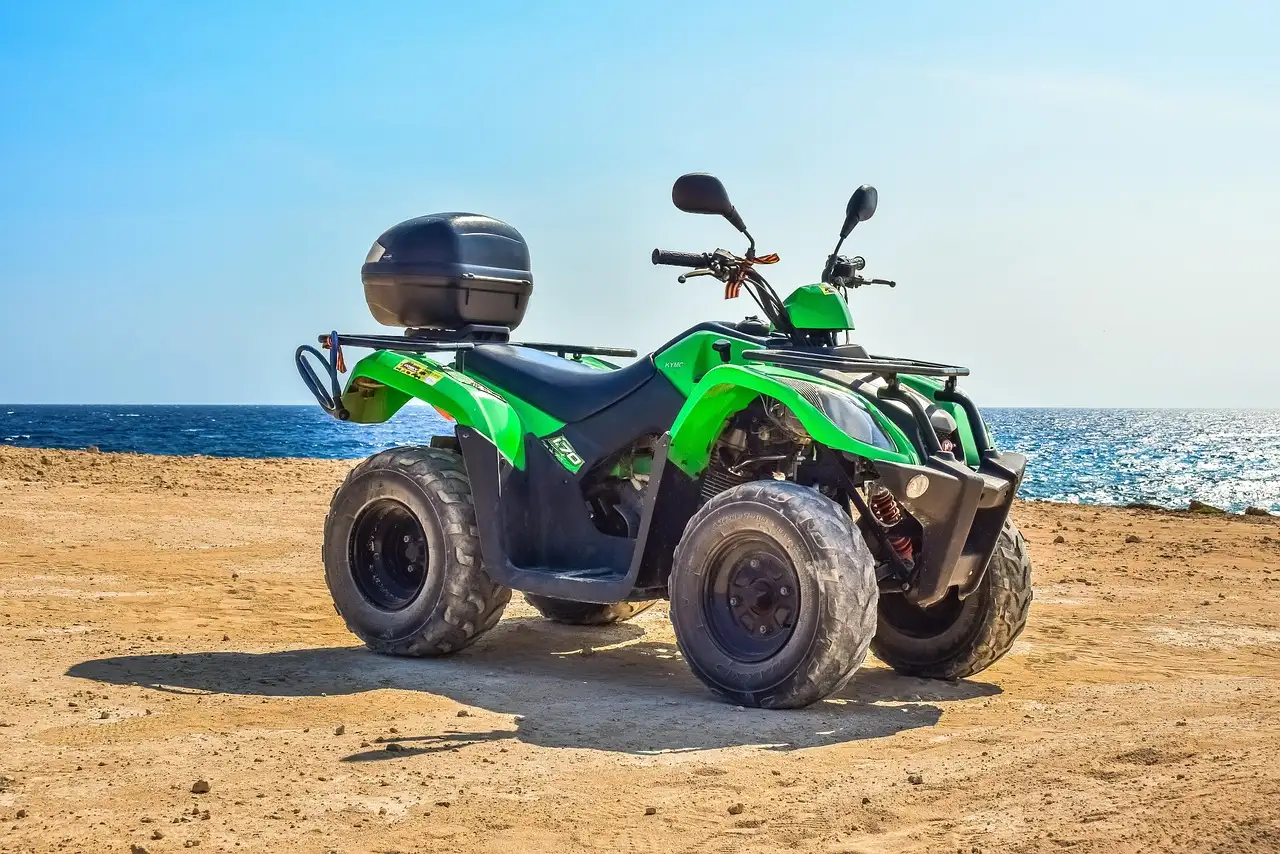 A green quad bike parked on a sandy track by the sea
