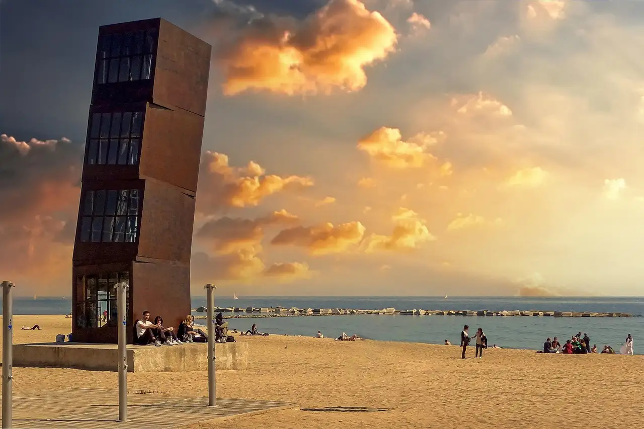 Sunset over the sand of Barceloneta beach in Barcelona, with the rusted steel L'Estel Ferit sculpture
