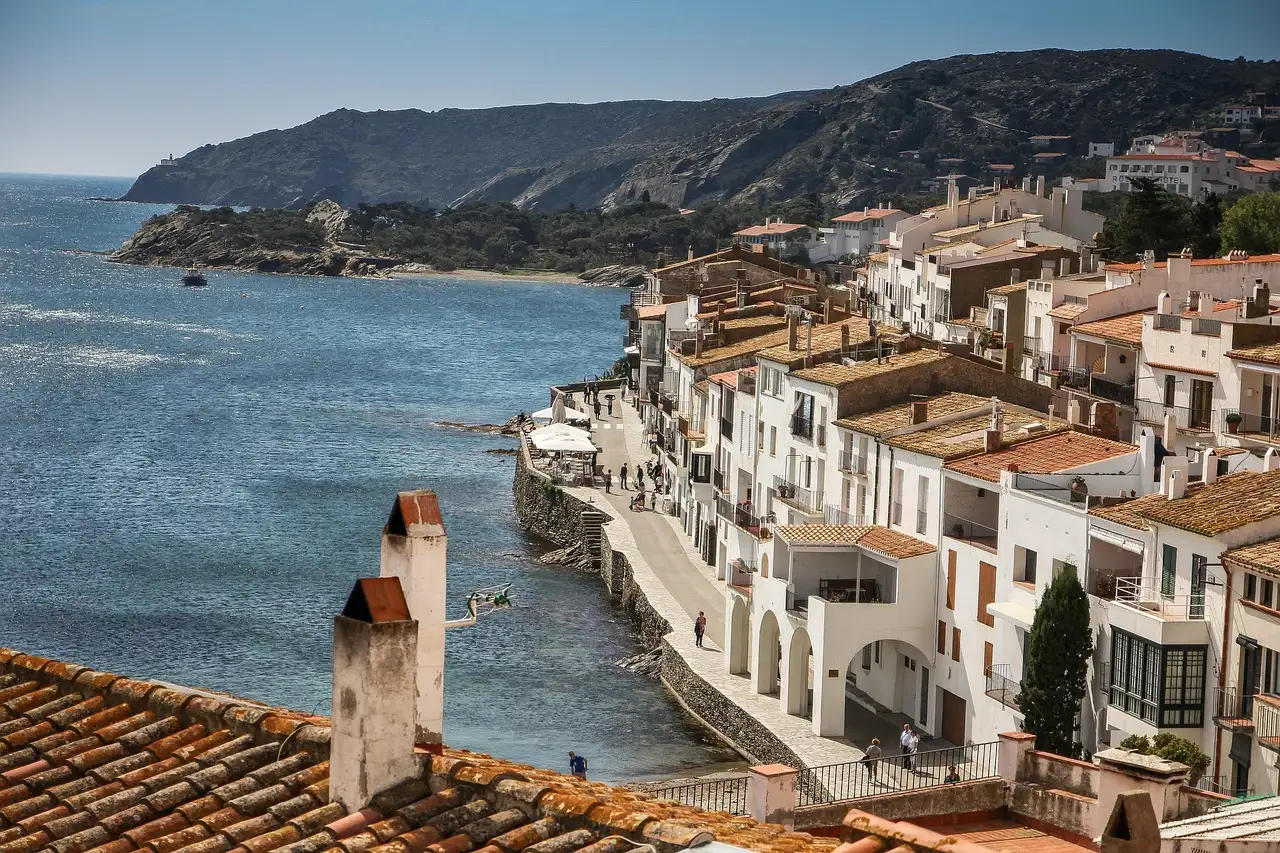 Rooftops and chimneys of Cadaqués above the sea, with a green headland behind