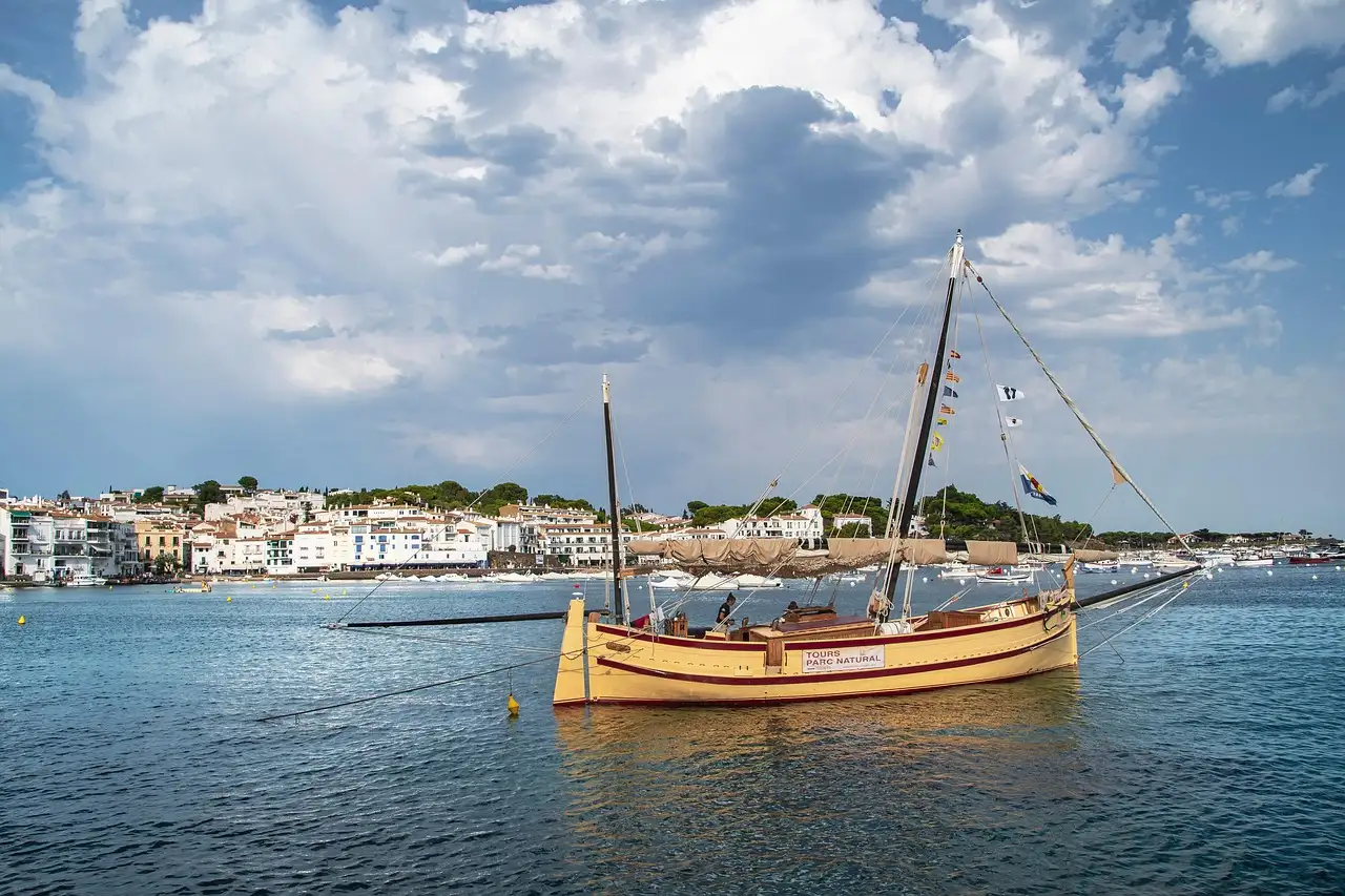 A wooden sailboat moored in the bay of Cadaqués, with the white town behind