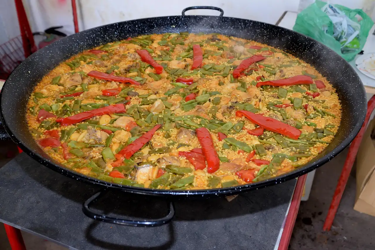 Large pan of paella with chicken, green beans and red pepper strips
