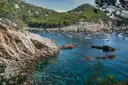 A rocky Costa Brava cove with clear water, pine trees and moored boats