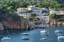 White houses above a rocky Costa Brava cove, with small boats moored in the water