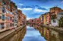 Tall painted houses reflected in the Onyar river in Girona, with a red iron bridge