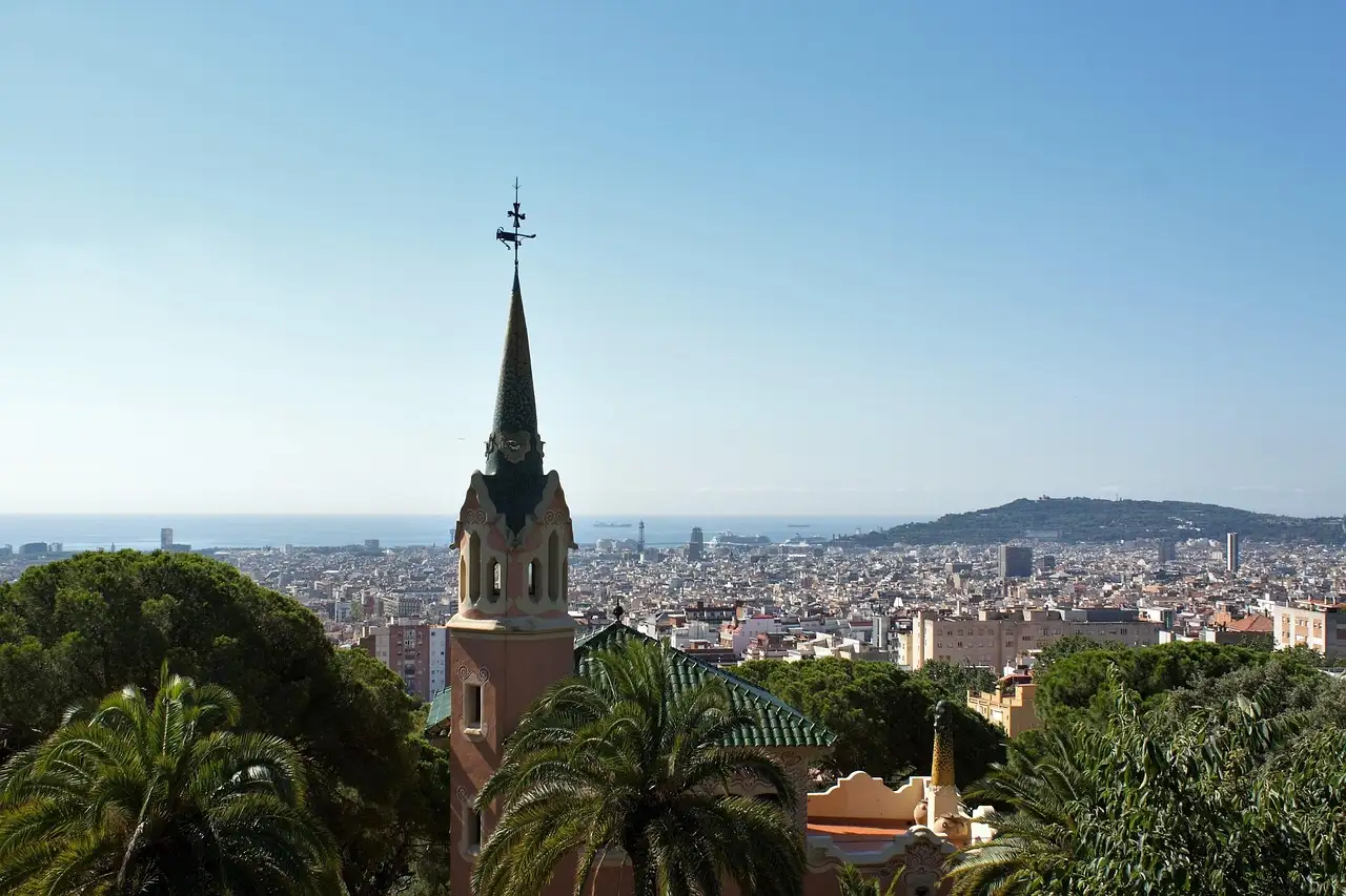 A pointed tower in Park Güell above the trees, with Barcelona and the sea behind