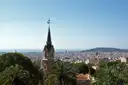 A pointed tower in Park Güell above the trees, with Barcelona and the sea behind