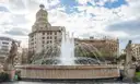 A fountain with stone statues on Plaça de Catalunya in Barcelona, with old buildings behind