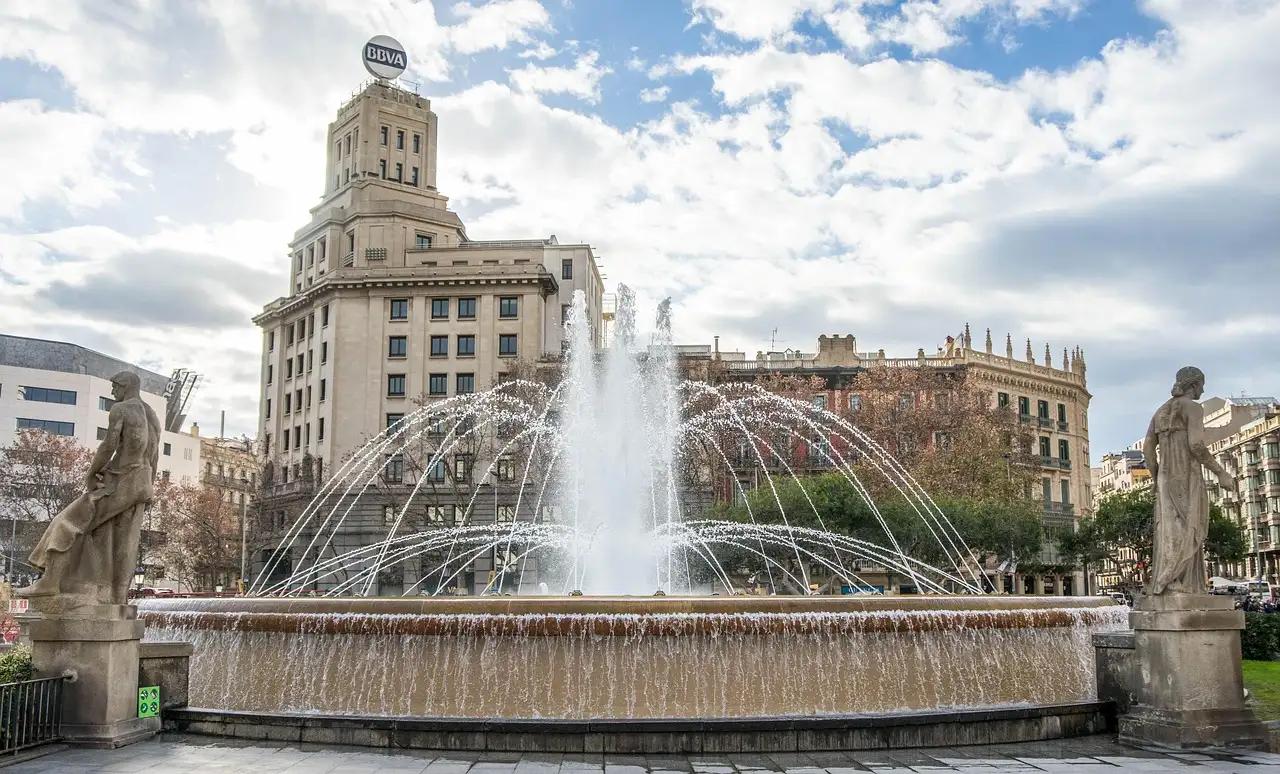 A fountain with stone statues on Plaça de Catalunya in Barcelona, with old buildings behind