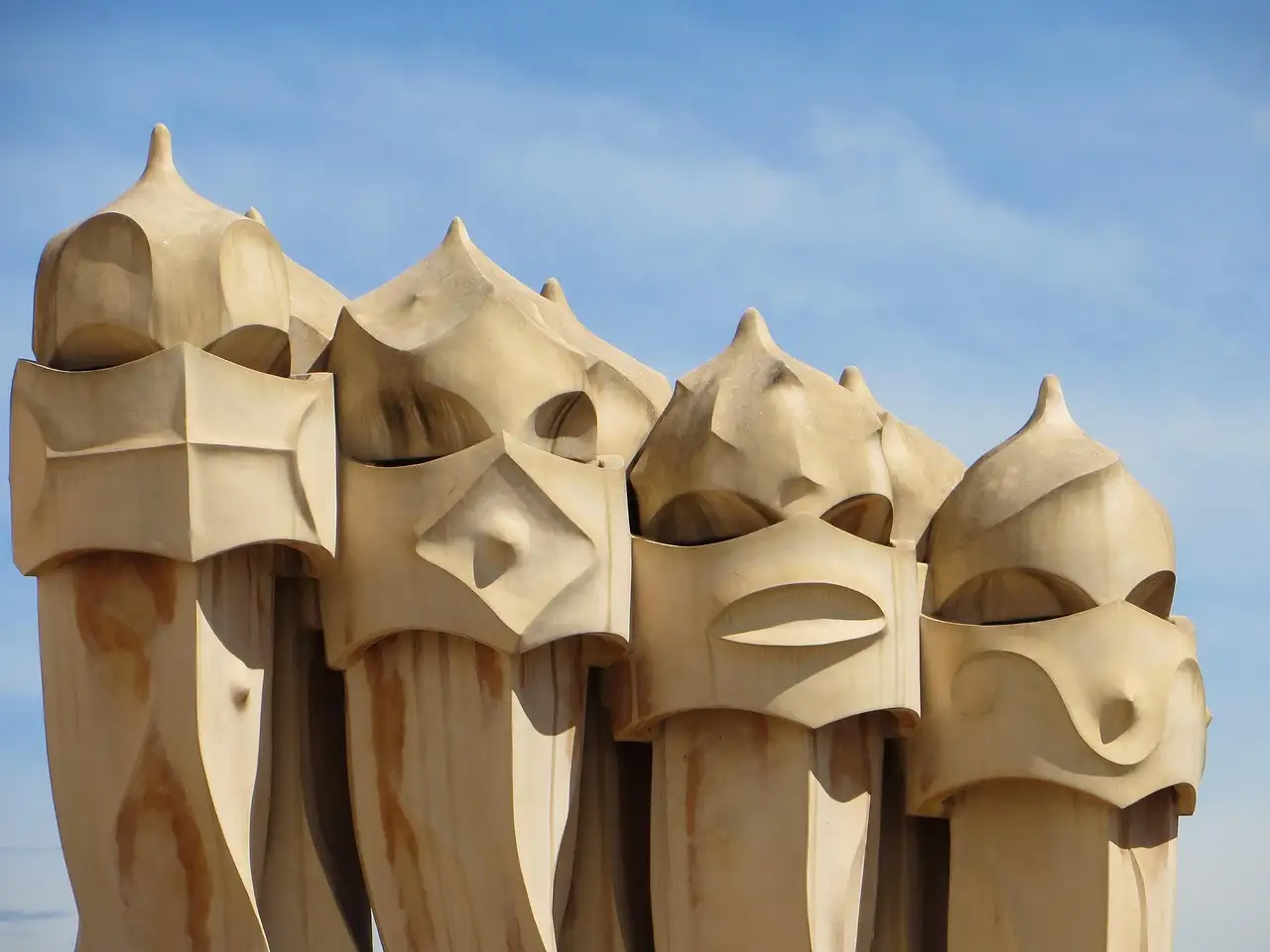 A row of tall, helmet-shaped chimneys on the roof of La Pedrera against a pale sky