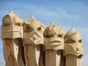 A row of tall, helmet-shaped chimneys on the roof of La Pedrera against a pale sky
