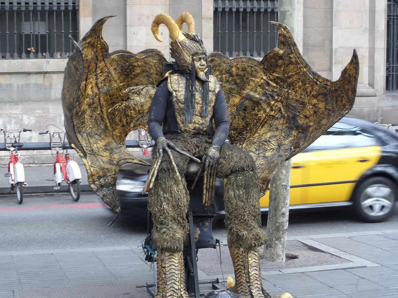 Living-statue street performer on La Rambla with a yellow and black taxi behind