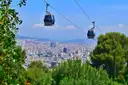 Montjuic cable car gondolas above pine trees with Barcelona and the Sagrada Familia below