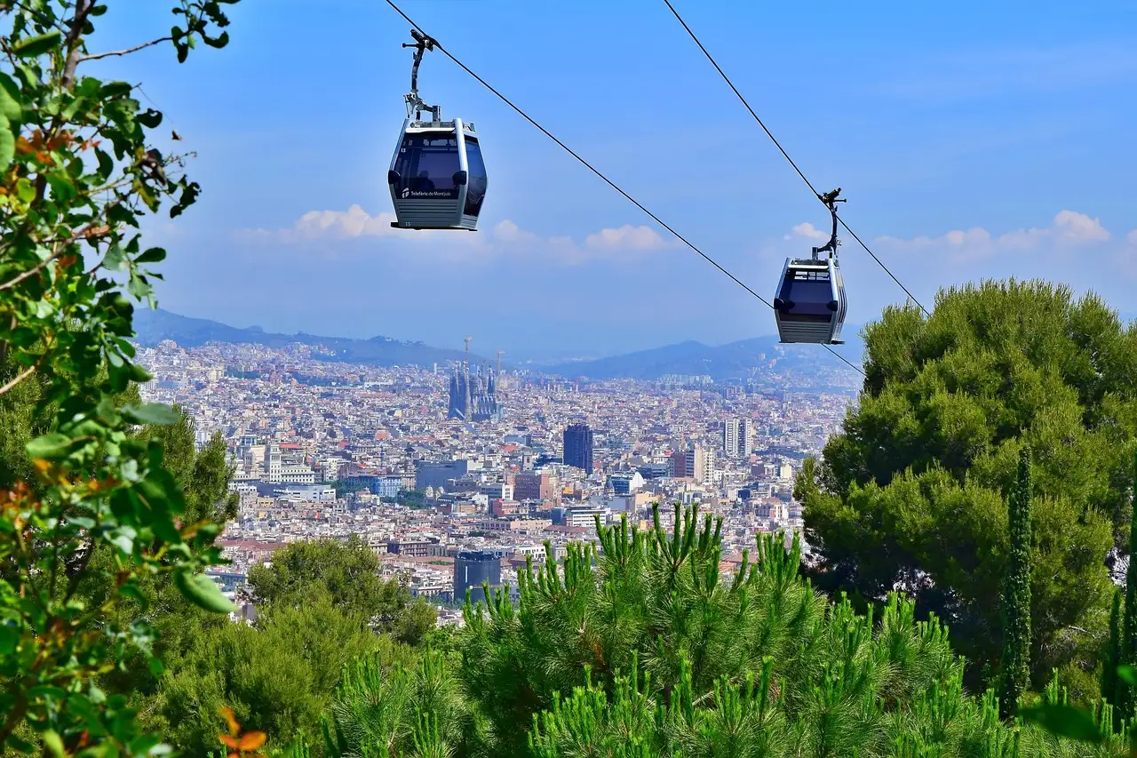 Montjuic cable car gondolas above pine trees with Barcelona and the Sagrada Familia below