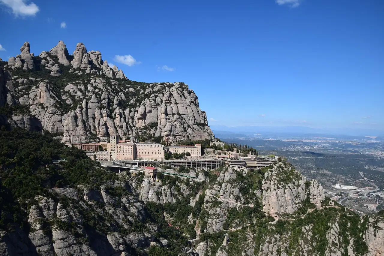 The Montserrat monastery buildings on a ledge below jagged rock peaks, under a blue sky