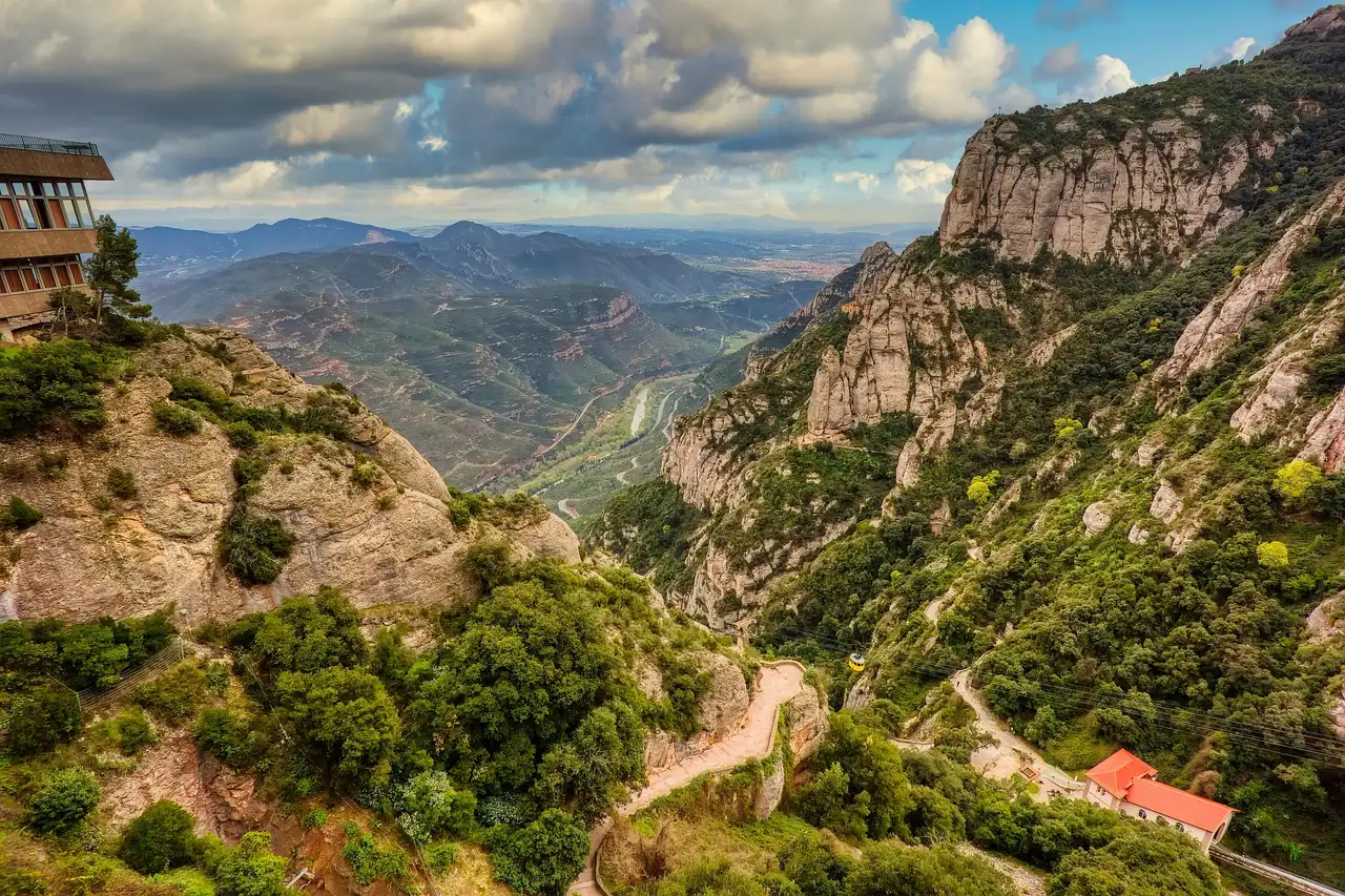 A winding mountain road below the rock walls of Montserrat, with wide valleys beyond