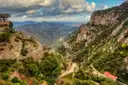 A winding mountain road below the rock walls of Montserrat, with wide valleys beyond