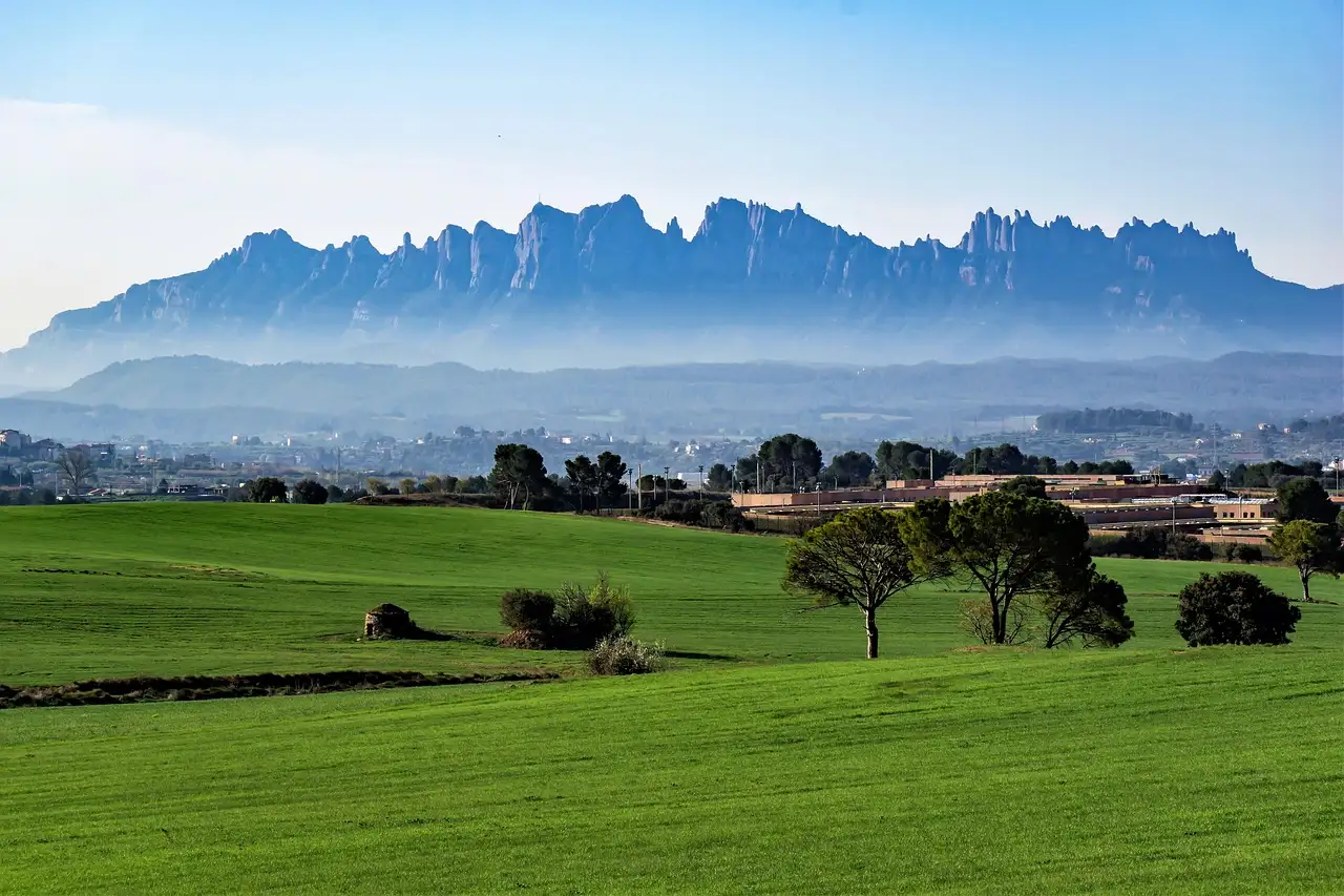 The jagged ridge of Montserrat above green fields and trees in the morning haze