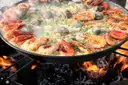Big paella pan with prawns and clams cooking over an open fire