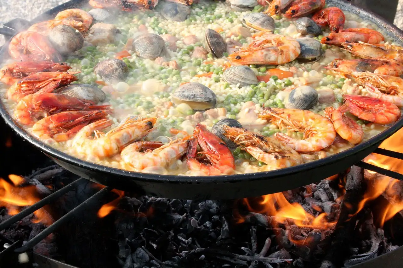 Big paella pan with prawns and clams cooking over an open fire