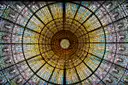 A round stained-glass skylight in gold, orange and blue, seen from below