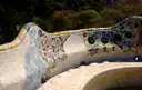 A long, wavy bench covered in white and colored broken tiles in Park Güell