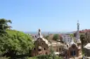 The Park Güell gatehouses among green trees, with the city and the sea behind