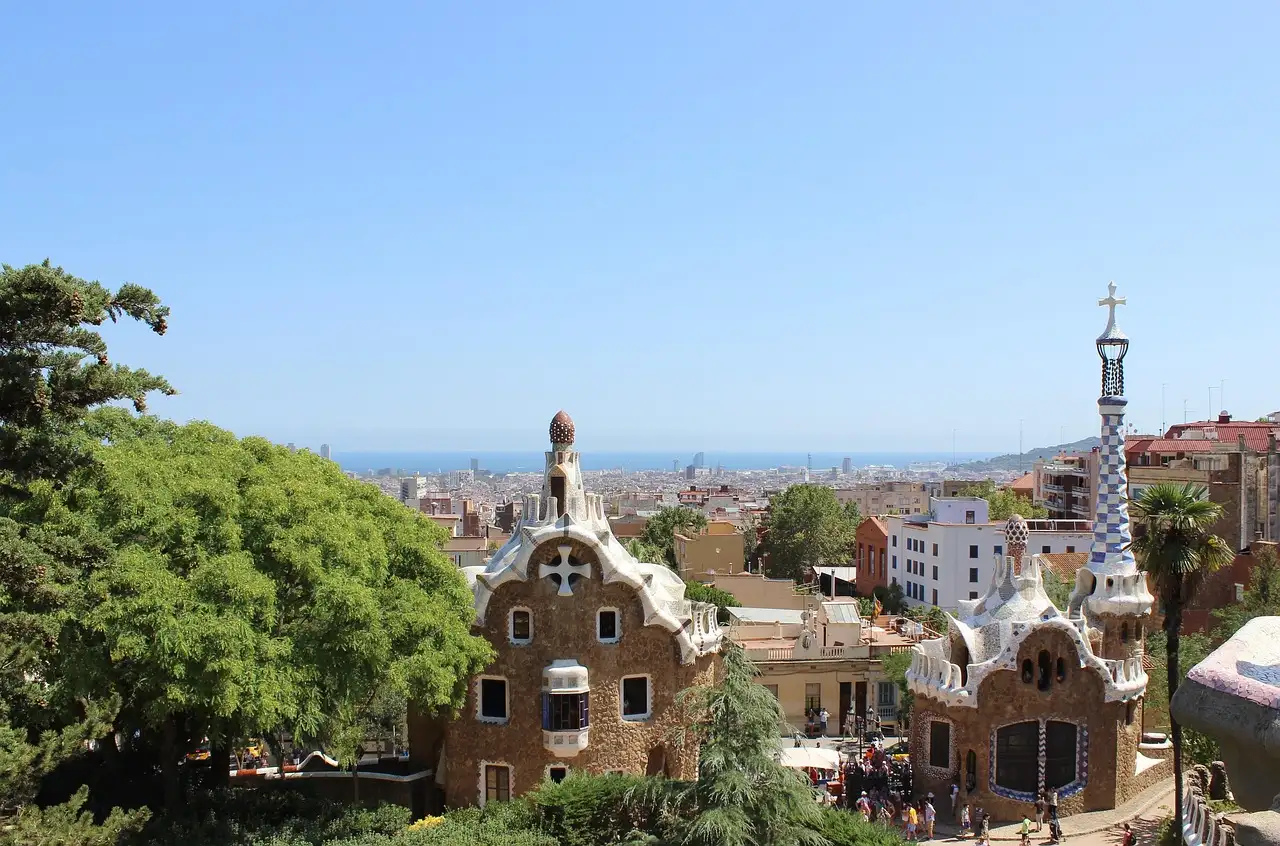 The Park Güell gatehouses among green trees, with the city and the sea behind