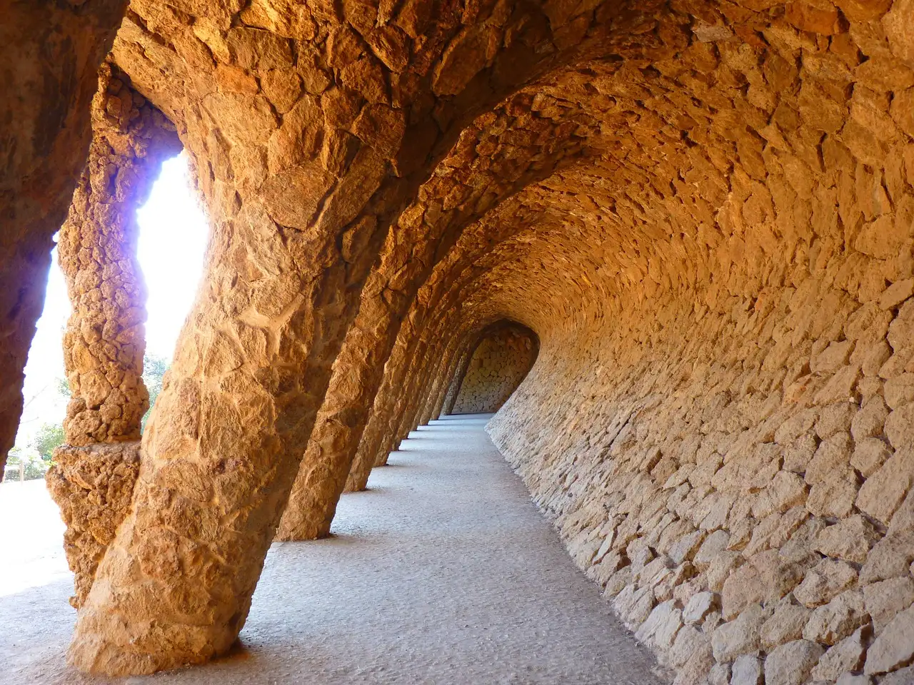A curving stone arcade with leaning columns in Park Güell