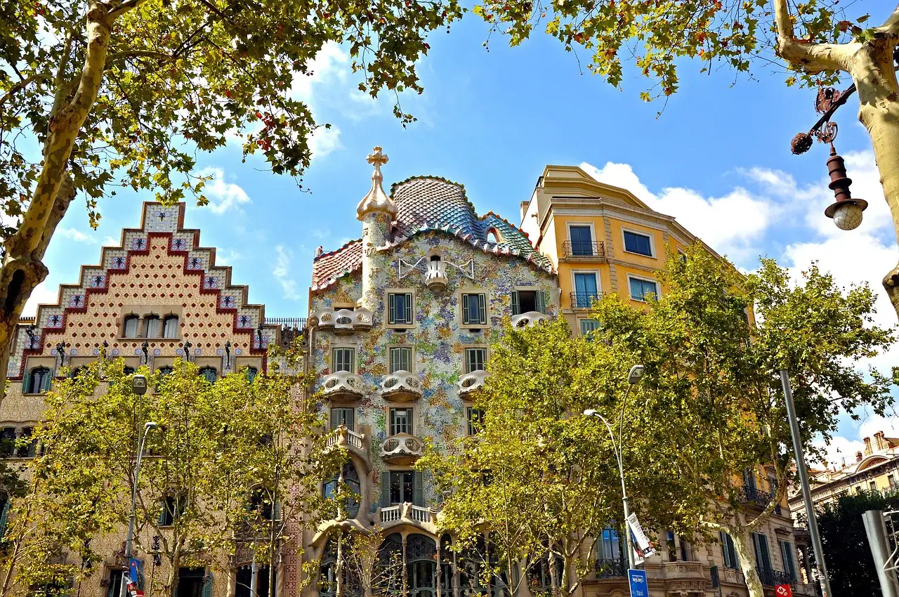 Casa Batlló and its neighbor on Passeig de Gràcia, framed by green trees and street lamps