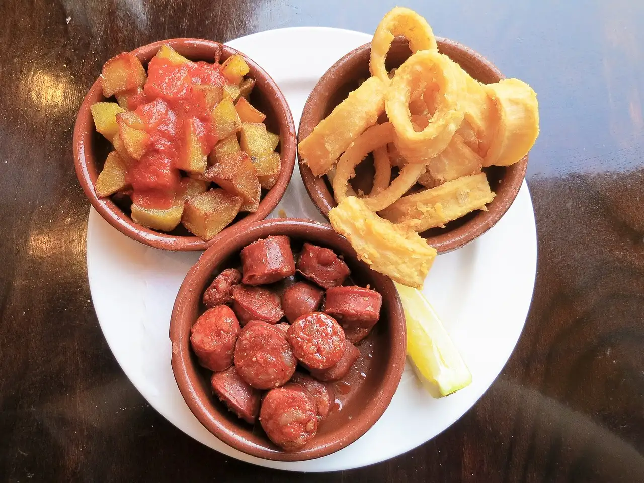 Tapas plate with potatoes in spicy sauce, fried squid rings and chorizo