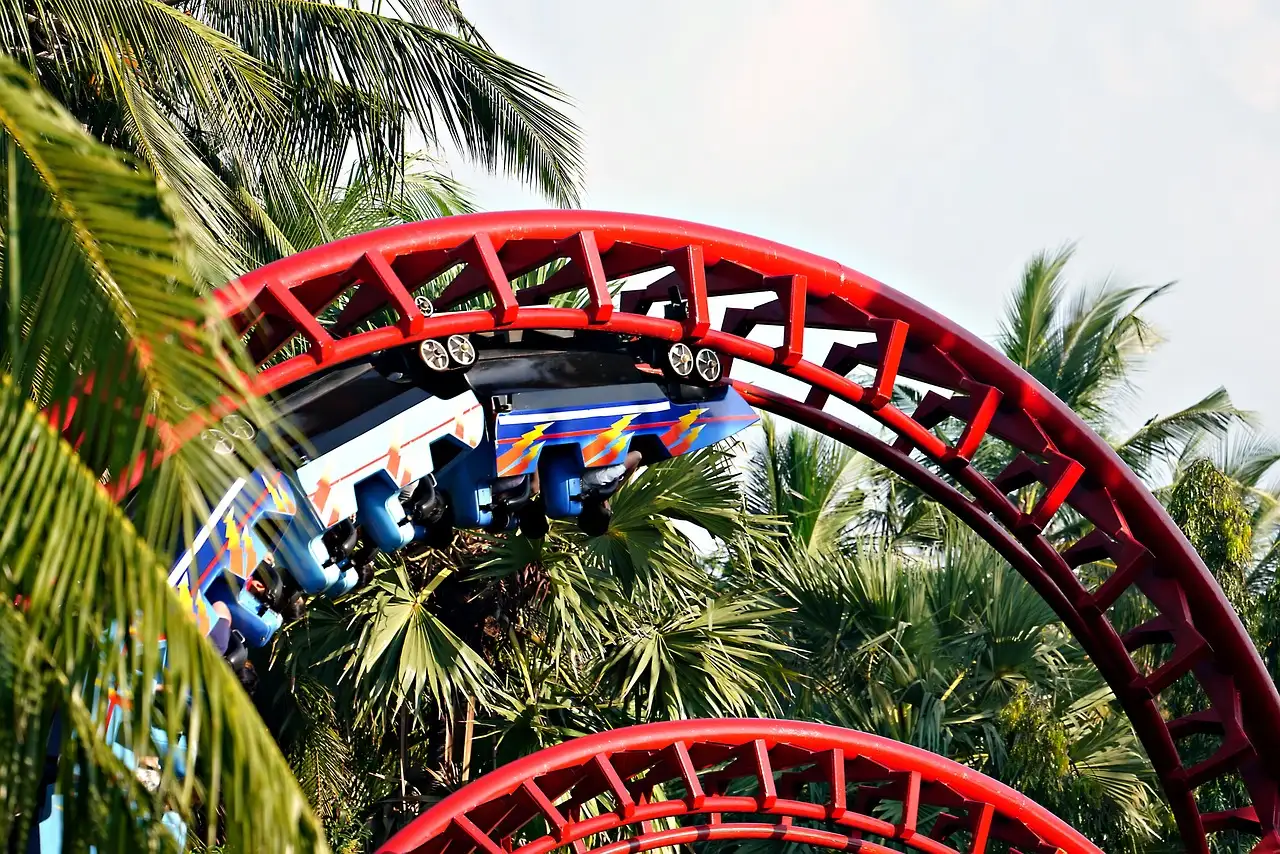 A red roller coaster loop between palm trees