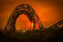 The loop of a roller coaster in silhouette against an orange sunset sky