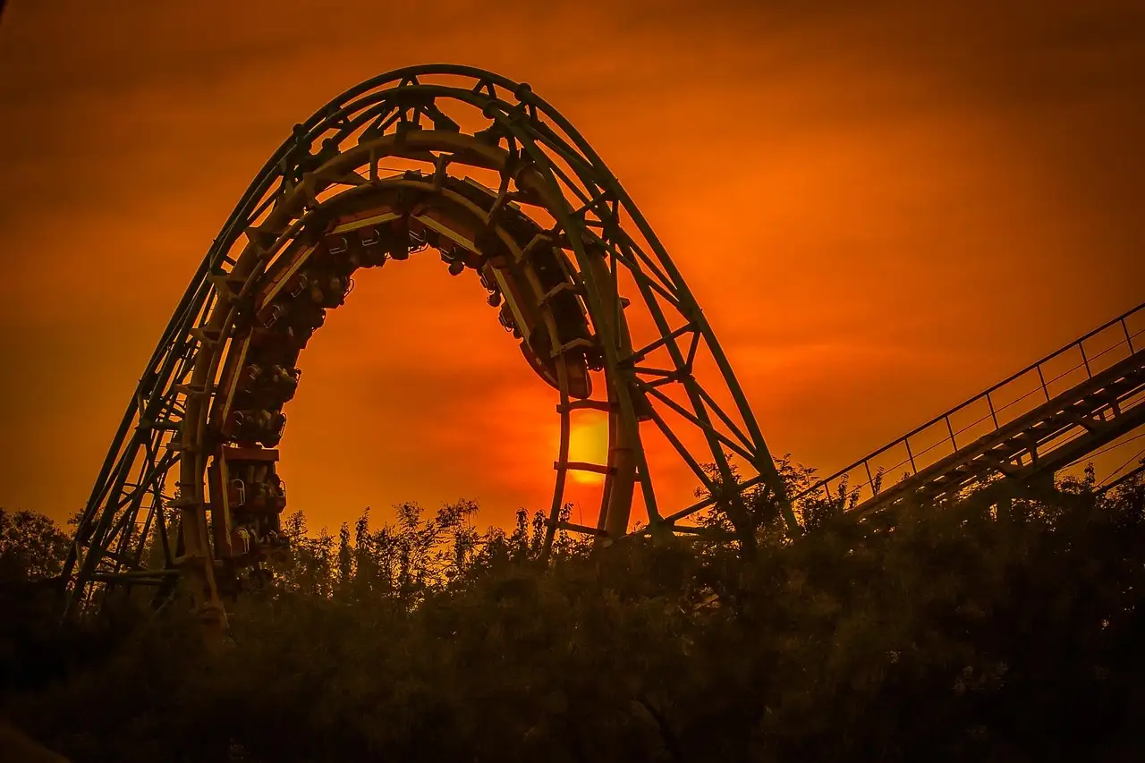 The loop of a roller coaster in silhouette against an orange sunset sky