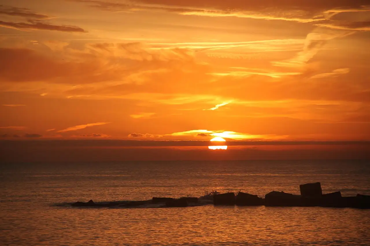Sunrise over the sea from a Barcelona beach, with a breakwater in silhouette