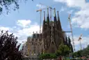 The Sagrada Família with building cranes beside its spires, behind green trees