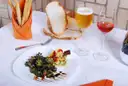 A plate of tapas with glasses of red wine and beer and bread on a white tablecloth