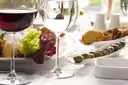Glass of red wine next to small plates of olives, toasts and salad