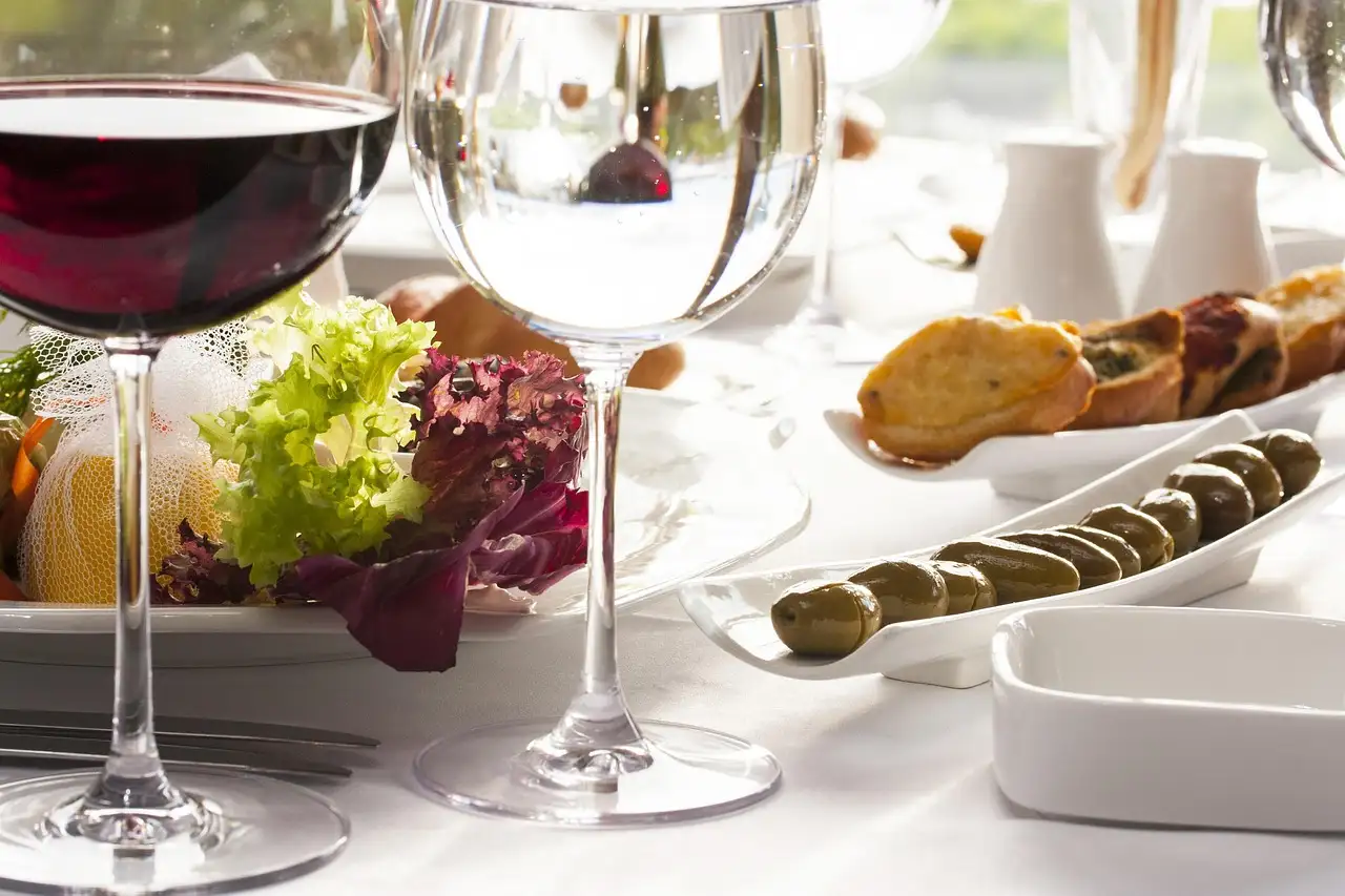Glass of red wine next to small plates of olives, toasts and salad
