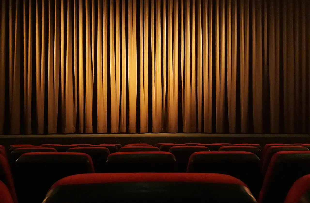 Lit stage curtain above rows of red theater seats