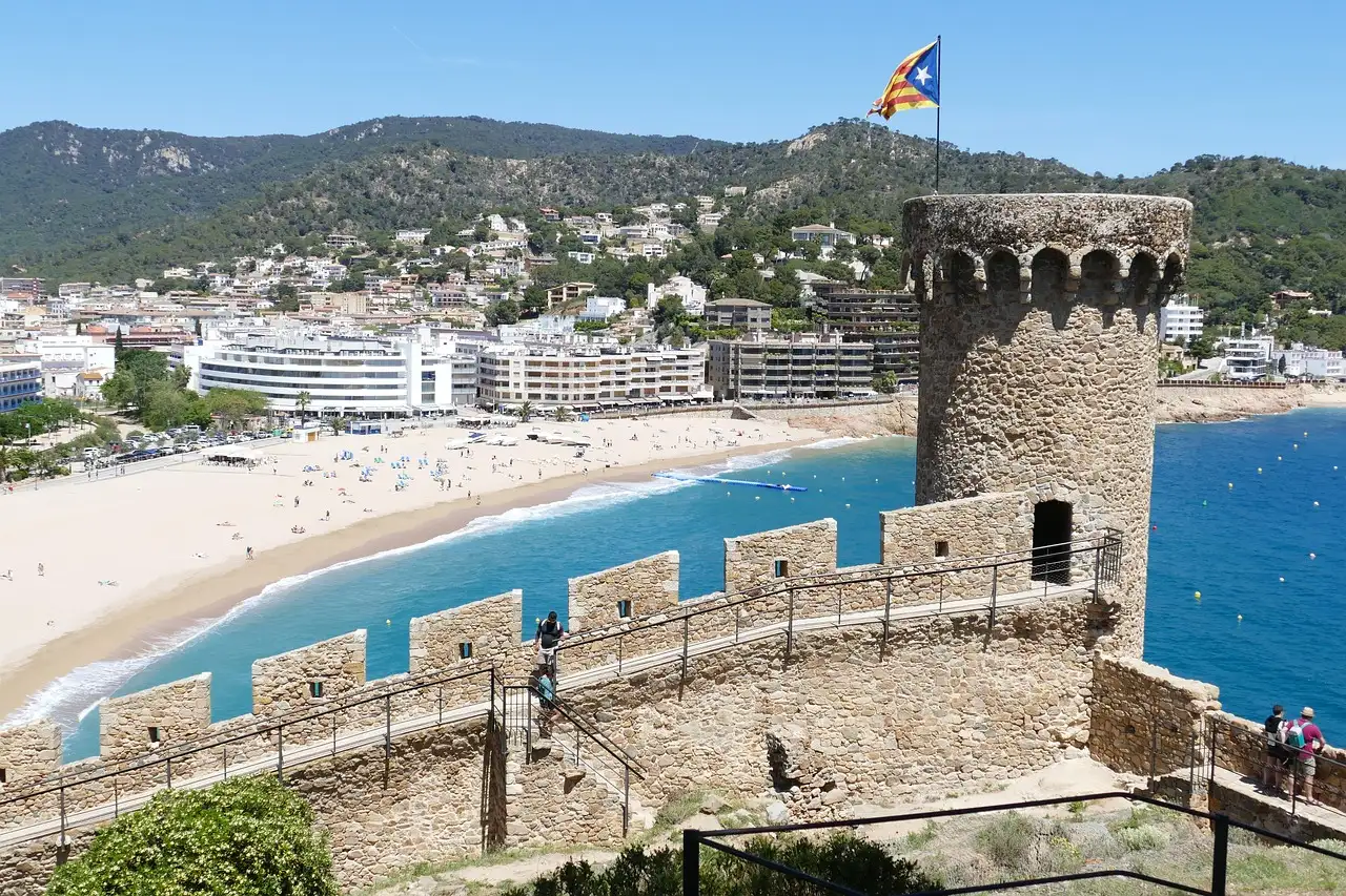The old walls and round tower of Tossa de Mar above a curved sandy beach