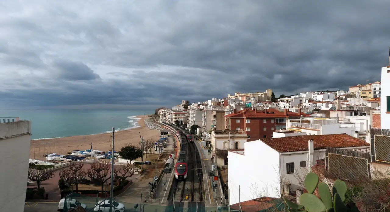 A railway line running along the beach of a Mediterranean coastal town in Catalonia under stormy skies