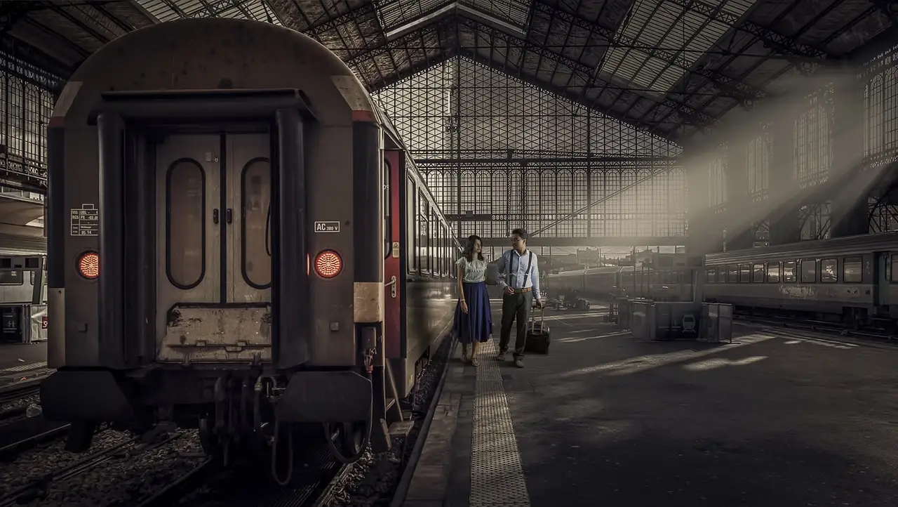 A couple with luggage on an old station platform beside a vintage train carriage