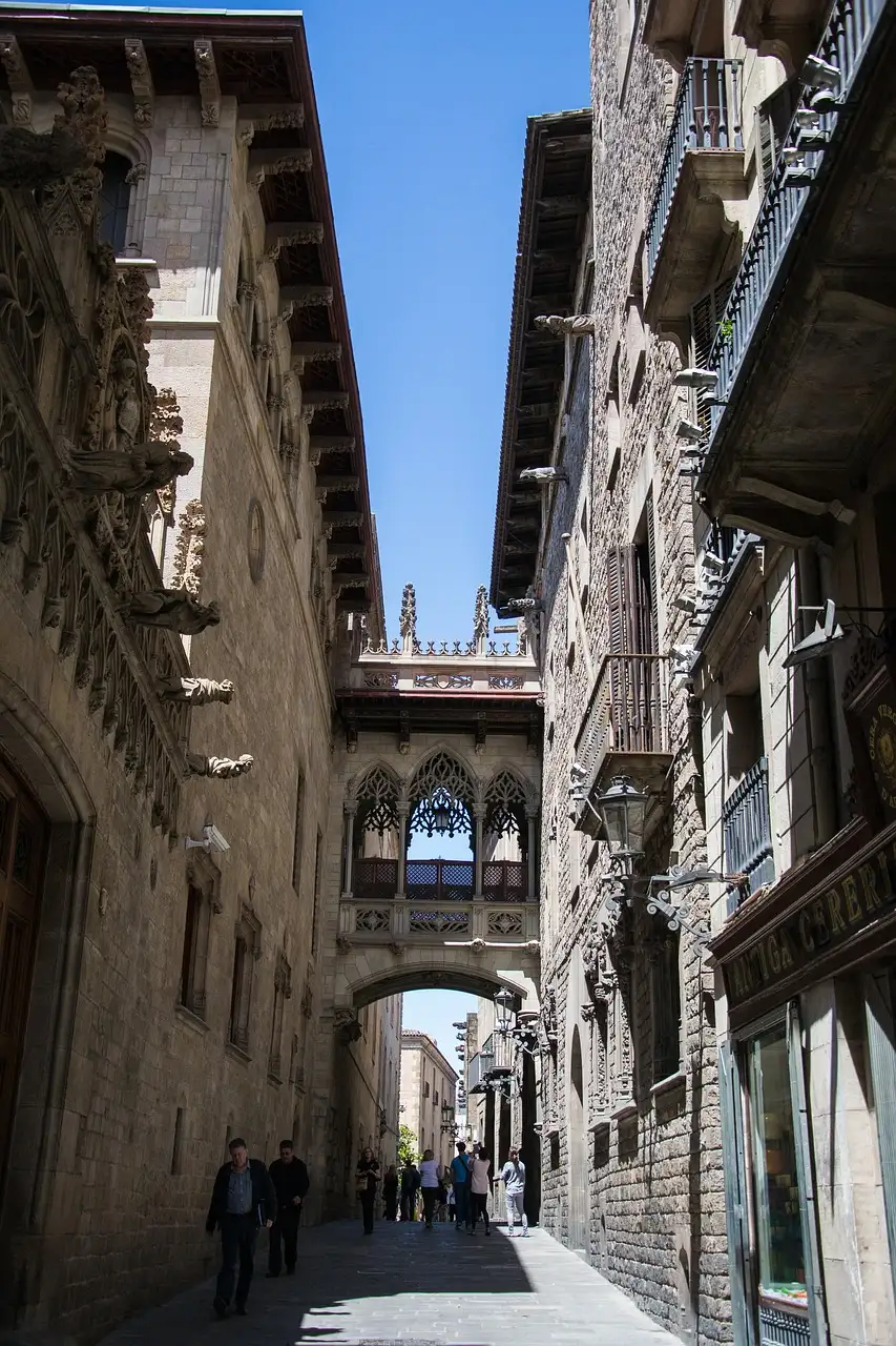 A narrow stone street in the Gothic Quarter with a carved bridge high across it